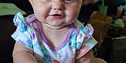 Dawn is registered to the contest to win money with this photo: arm, baby, blue_eyes, blurred_background, child, closeup, cute, face, floral_clothing, furniture, hand, happy, holding, indoor, infant, person, sitting, skin, smile, young