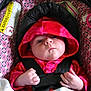 baby, child, car_seat, hood, red_clothing, infant, seatbelt, patterned_fabric, indoor, cute, face, person, young_child, hands, straps, closeup, child_in_car_seat, baby_clothes, expression, sitting