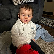 Elijah joined the competition — help win amazing prizes! toddler, child, smiling, indoor, hoodie, plush_toy, carpet, sofa, pillow, blanket, floor, person, happy, cozy, clothing, toy, home, cute, sitting, living_room
