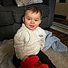 toddler, child, smiling, indoor, hoodie, plush_toy, carpet, sofa, pillow, blanket, floor, person, happy, cozy, clothing, toy, home, cute, sitting, living_room
