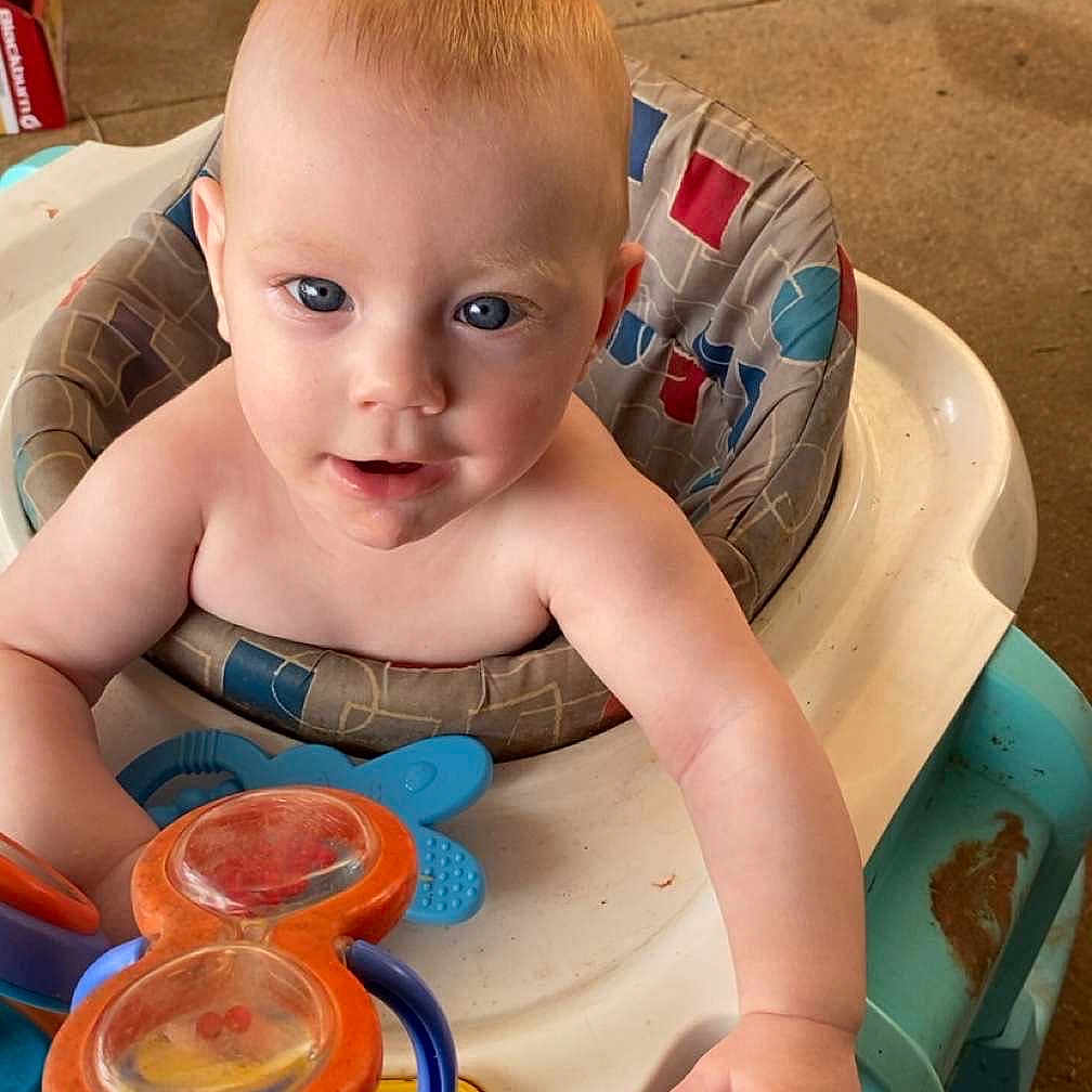 Jensen is registered to the contest to win money with this photo: baby, walker, toy, blue_eyes, indoor, child, person, plastic, colorful, curious, seat, playtime, floor, garage, tools, bicycle, hand, expression, infant, cute