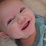 Walker is registered to the contest to win money with this photo: baby, smiling, face, child, infant, blue_shirt, blanket, soft_texture, happy, cute, portrait, closeup, skin, head, eyes, mouth, person, lying_down, cozy, joyful