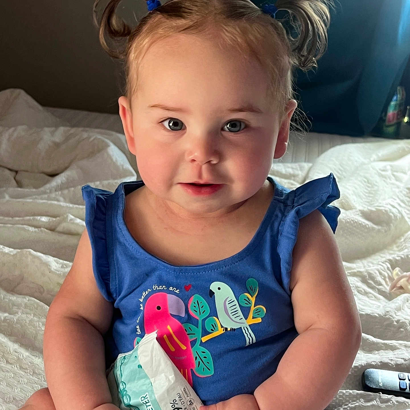 Alona joined the competition — help win amazing prizes! toddler, child, baby, portrait, sitting, bed, bedroom, pigtails, blue_dress, smiling, face, eyes, indoor, snack_bag, toy_lid, blanket, bedding, remote_control, daylight, close_up