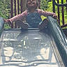 child, daylight, face, forest, happy, laughing, metal_slide, nature, outdoor, overalls, pink_shirt, playground, playground_equipment, portrait, railings, shoes, sitting, slide, smiling, toddler