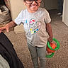 bedroom, braids, carpet, casual_clothing, child, colorful, educational_toy, family, girl, glasses, happy, home, indoors, playtime, portrait, puzzle, smiling, standing, toddler, toy