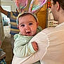 baby, bunny_ears, blue_eyes, child, cute, family, home, indoor, person, woman, man, holding, smile, pastel_colors, carpet, refrigerator, glasses, earrings, sleeve, doorway