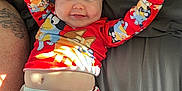 Makenna joined the competition — help win amazing prizes! baby, smiling, pajamas, red_clothing, cartoon_characters, bed, gray_bedspread, happy, arms_up, tattoo, diaper, infant, child, face, cheeks, cute, lying_down, person, indoor, sleepwear