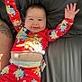 baby, smiling, pajamas, red_clothing, cartoon_characters, bed, gray_bedspread, happy, arms_up, tattoo, diaper, infant, child, face, cheeks, cute, lying_down, person, indoor, sleepwear