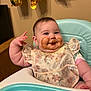 baby, high_chair, bib, food_mess, smile, cheeks, hand, face, blue_eyes, floral_pattern, indoor, table, celebration, gold_balloon, cute, child, infant, messy, happy, portrait