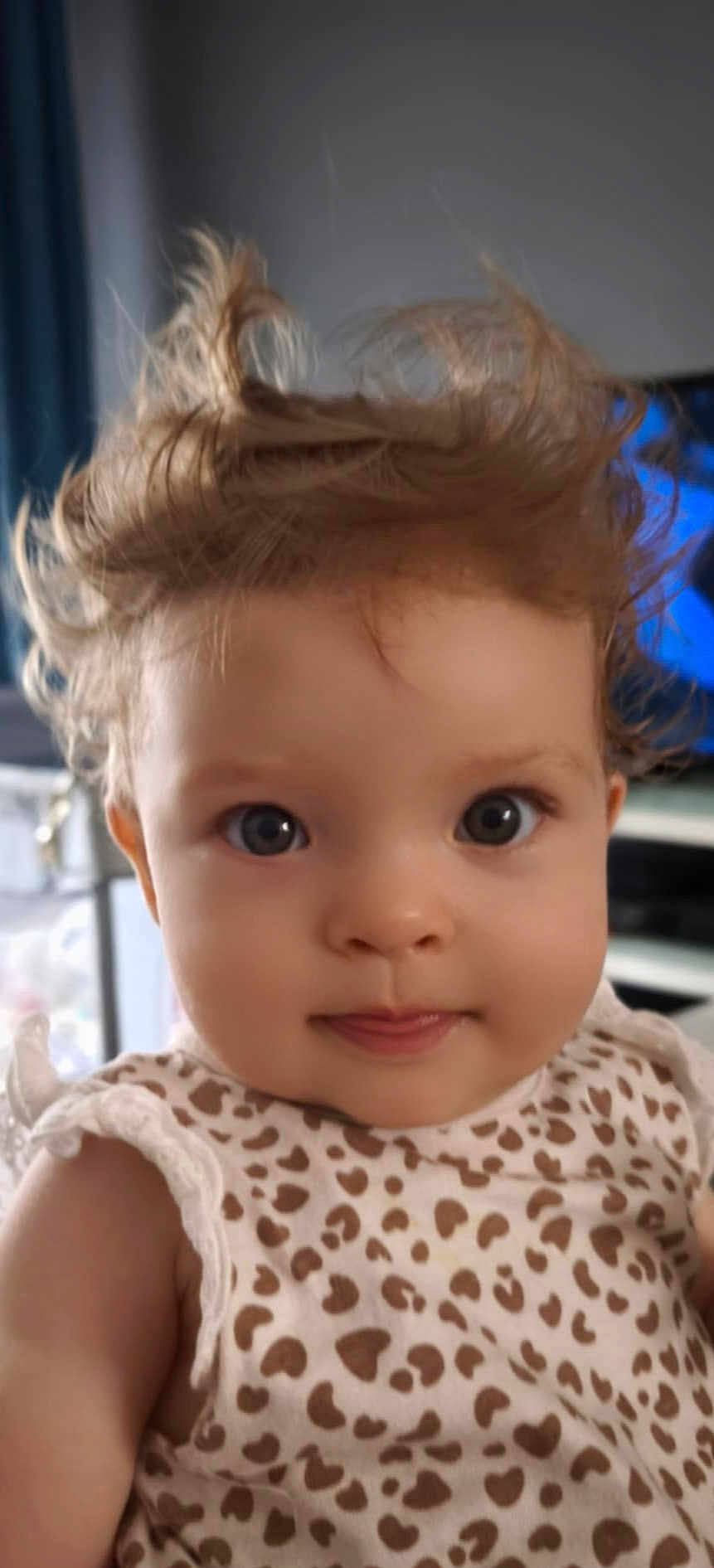 Mia participe au concours pour gagner de l'argent avec cette photo : baby, child, face, hair, curly_hair, blue_eyes, dress, pattern, heart_pattern, indoor, portrait, cute, closeup, smile, infant, young_child, person, apparel, soft_lighting, expression
