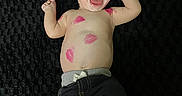 Elias is registered to the contest to win money with this photo: baby, child, smiling, lipstick, kiss_marks, face, bare_chest, black_background, pants, happy, lying_down, cute, infant, skin, expression, joyful, hands, feet, young, playful