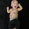 baby, child, smiling, lipstick, kiss_marks, face, bare_chest, black_background, pants, happy, lying_down, cute, infant, skin, expression, joyful, hands, feet, young, playful