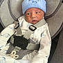 baby, infant, car_seat, blue_hat, mummys_boy, white_outfit, baby_clothing, straps, seatbelt, cute, face, portrait, newborn, child, indoors, soft_fabric, sitting, attention, expression, safety