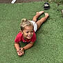 child, smiling, grass, artificial_turf, barefoot, red_shirt, shorts, outdoor, playful, happy, young, person, footwear, sandals, dirt, grass_patch, casual, summer, childhood, relaxed