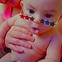 baby, child, adult, hand, sunglasses, star_shaped, face, skin, expression, holding, curious, mouth_open, person, closeup, indoor, warm_light, colorful, soft_focus, parent, interaction