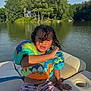 Bronx is registered to the contest to win money with this photo: child, boy, lake, boat, life_jacket, water, summer, swimwear, sunlight, trees, outdoor, nature, water_sports, curly_hair, seat, recreation, vacation, sunny, young, daytime