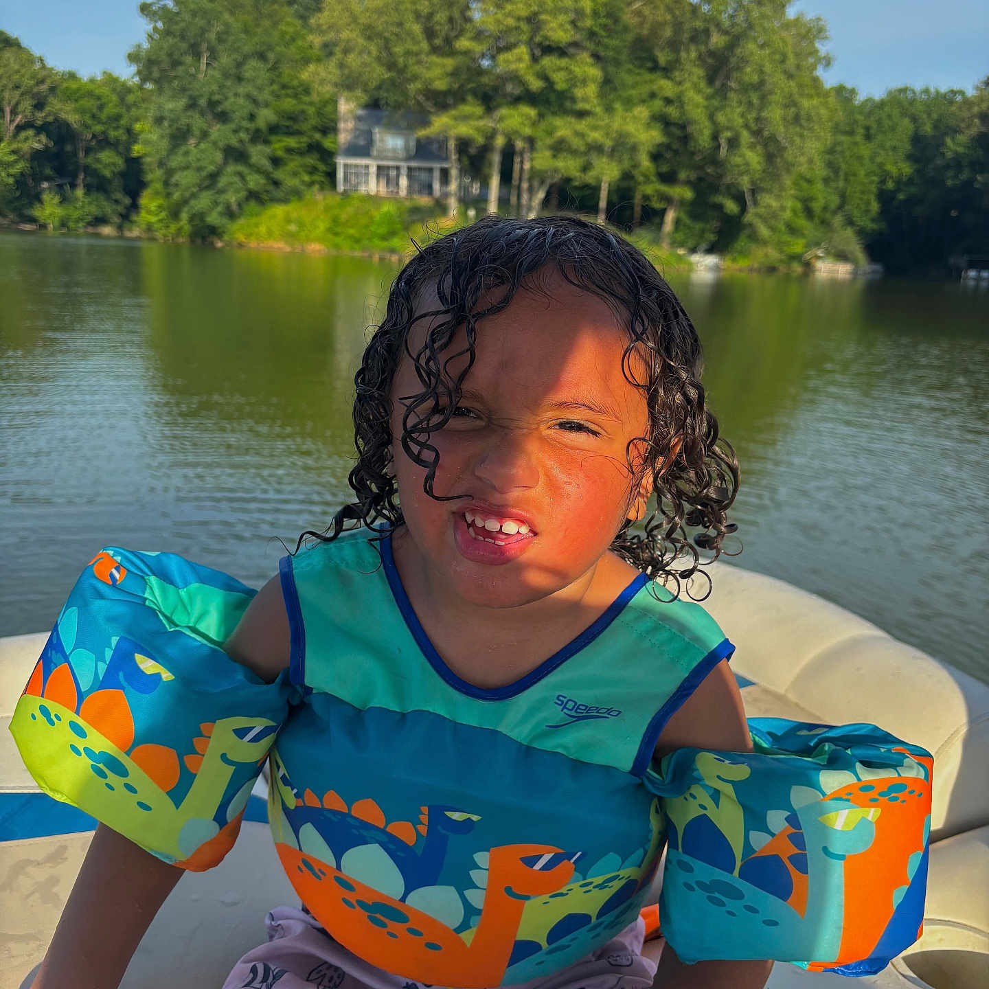 Bronx joined the competition — help win amazing prizes! boat, boy, child, curly_hair, dinosaur_print, floatation_device, funny_face, house, lake, life_jacket, nature, outdoor, recreation, sitting, summer, sunlight, trees, water, water_safety, wet_hair