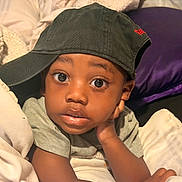 Royal is registered to the contest to win money with this photo: toddler, child, face, cap, hat, blanket, pillow, bed, curious, expression, indoor, person, casual_clothing, skin, portrait, resting, cozy, young, cute, relaxed