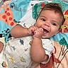 Callum is registered to the contest to win money with this photo: baby, infant, smiling, hands, play_mat, toy, colorful, cute, cheerful, lying_down, dinosaur_print, onesie, bright, happy, child, indoors, soft_toy, playful, face, expression