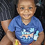 toddler, child, smiling, blue_tshirt, orange_shorts, car_seat, inside_car, pacifier, snack, hands, legs, curly_hair, person, seat, window, daylight, vehicle, happy, casual_clothing, portrait