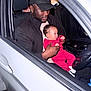 man, baby, car, black_cap, red_clothing, holding, seat, interior, window, steering_wheel, night, portrait, child, parent, affection, casual_clothing, curly_hair, beard, seatbelt, automobile