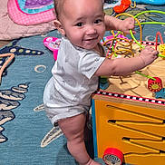 Octavia joined the competition — help win amazing prizes! baby, child, toy, bead_maze, play, colorful, rug, indoors, smile, standing, blanket, furniture, wooden_toy, floor, person, cute, happy, playroom, foot, hand
