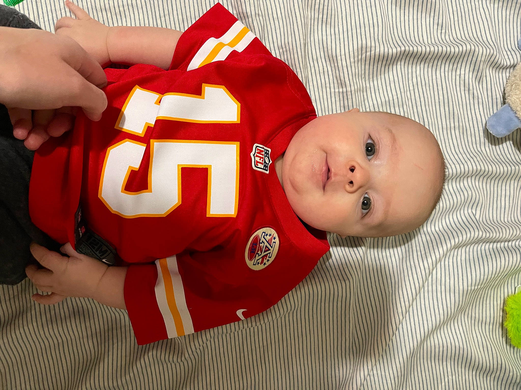 Baylor is registered to the contest to win money with this photo: baby, baby_toddler_clothing, carmine, child, comfort, flooring, grass, jersey, pattern, person, sleeve, sports_gear, sports_jersey, sports_uniform, sportswear, thumb, toddler, wood