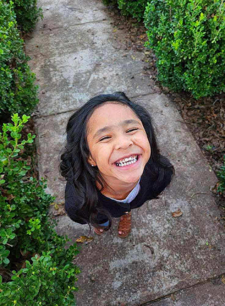 Jadiah joined the competition — help win amazing prizes! child, girl, smiling, happy, outdoor, greenery, bushes, sidewalk, path, nature, portrait, cute, young, person, long_hair, casual_clothing, daylight, feet, sandals, joy