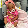 baby, sleeping, pacifier, headband, pink_outfit, blanket, car_seat, infant, cute, child, soft_texture, clothing, resting, adorable, indoors, comfort, newborn, toddler, accessory, peaceful