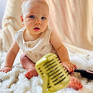 Léïo a rejoint le concours — aidez-le/la à gagner de superbes lots ! baby, blue_eyes, microphone, blanket, infant, cute, child, indoor, soft_texture, curious, portrait, musical_instrument, vintage_microphone, sitting, cozy, clothing, hand, foot, expression, background