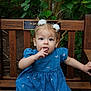 child, toddler, baby, bench, wooden_bench, blue_dress, hair_bows, fingers_in_mouth, sitting, portrait, outdoors, garden, greenery, foliage, curious, cute, candid, person, nature, plush