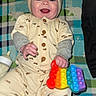 Nova joined the competition — help win amazing prizes! baby, child, infant, smiling, hat, bear_ears, pajamas, toy, pop_it, bottle, blanket, plaid, colorful, indoor, cute, happy, playful, clothing, hand, face