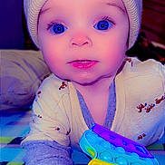 Nova is registered to the contest to win money with this photo: baby, child, blue_eyes, hat, knit_hat, pom_poms, toy, pop_it, rainbow_colors, blanket, checkered, cute, infant, indoor, portrait, face, hand, clothing, expression, lying_down