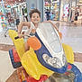 child, smiling, mall, shopping_mall, ride, motorcycle_ride, toy, colorful, curly_hair, happy, indoor, playful, person, storefront, shoppers, floor, clothing, handlebars, fun, retail