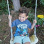 child, curly_hair, swing, outdoor, garden, tree, greenery, grass, smiling, happy, tshirt, shorts, play, rope, seat, nature, daylight, person, fun, leisure