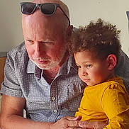 Lucas a rejoint le concours — aidez-le/la à gagner de superbes lots ! elderly_man, child, indoor, curly_hair, yellow_shirt, sunglasses, gentle_touch, family, intense_gaze, human, portrait, candid, affection, casual_clothing, beard, short_sleeves, light_skin, brown_skin, tender_moment