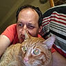 man, cat, orange_tabby, indoor, selfie, close_up, striped_fabric, couch, pet, feline, person, casual_clothing, relaxed, whiskers, fur, eyes, head, face, comfort, home