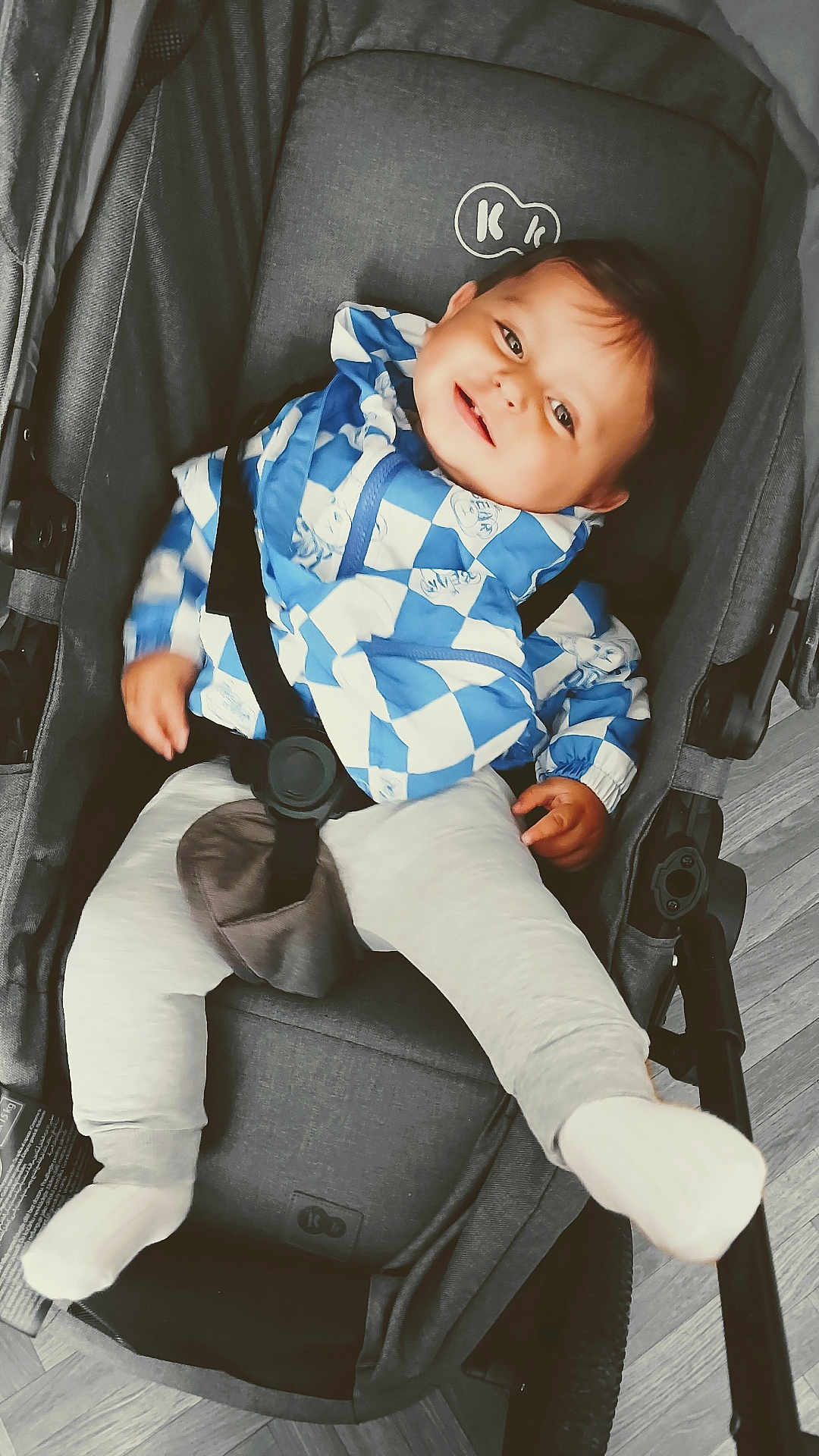 Ahmed participe au concours pour gagner de l'argent avec cette photo : toddler, child, stroller, jacket, blue_and_white, smiling, happy, face, white_socks, gray, seatbelt, indoor, floor, wood_floor, clothing, person, baby, casual, cute, portrait