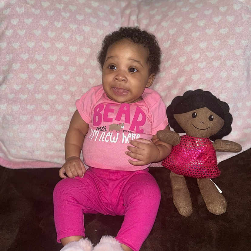Zakiyah is registered to the contest to win money with this photo: baby, clothing, couch, cushion, doll, face, footwear, furniture, head, homedecor, pants, person, photography, pillow, plush, portrait, shoe, sitting, t_shirt, toy