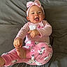 baby, child, pink_clothing, headband, hello_kitty, pajamas, foot, hand, bed, grey_bedspread, smiling, happy, infant, cute, lying_down, playful, indoors, person, young_child, cozy
