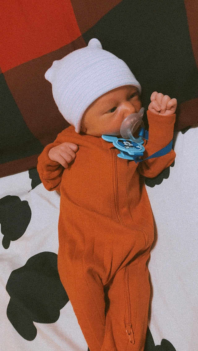 Aspen is registered to the contest to win money with this photo: baby, infant, pacifier, onesie, hat, sleepwear, blanket, lying_down, newborn, child, cute, indoors, soft_lighting, sleepy, resting, close_up, small_hands, face, person, cozy