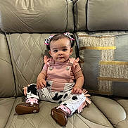 Erica is registered to the contest to win money with this photo: baby, child, comfortable, couch, cow_print, cute, decor, face, furniture, hair_bows, home, indoor, infant, leather, person, pillow, pink_clothing, shoes, sitting, smile