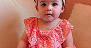 Erica is registered to the contest to win money with this photo: baby, child, coral, couch, curious, cute, dress, flower, footwear, girl, headband, indoor, lace, peach, person, portrait, sitting, toddler, wall, white_shoes