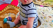 Hudson joined the competition — help win amazing prizes! baby, child, toddler, sitting, tongue_out, smiling, portrait, playroom, toys, blanket, cushion, carpet, socks, striped_shirt, infant, indoors, colorful, nursery, toy_storage, happy