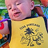 Hudson is registered to the contest to win money with this photo: baby, child, infant, smiling, happy, portrait, face, dinosaur, yellow_outfit, onesie, play_mat, toy, plush_toy, outdoor, lying_down, colorful, close_up, hand, lock_screen, phone_screenshot