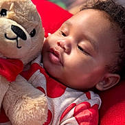 Jordan is registered to the contest to win money with this photo: baby, teddy_bear, plush_toy, red_bow, red_blanket, infant, soft_toy, close_up, child, cute, portrait, curly_hair, sleepwear, heart_pattern, indoor, comfort, cuddly, face, young_child, toddler
