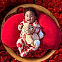 baby, child, teddy_bear, red_cushion, wooden_bowl, rose_petals, heart_pattern, pajamas, smiling, cute, indoor, plush_toy, portrait, cozy, comfort, infant, relaxing, soft_texture, bright_colors, adorable