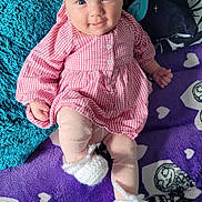 Maeve joined the competition — help win amazing prizes! baby, child, smiling, pink_dress, headband, bow, blanket, pillow, purple_blanket, white_booties, cozy, indoor, cute, infant, lying_down, patterned_blanket, soft_texture, happy, person, portrait