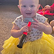 Sage is registered to the contest to win money with this photo: baby, child, toy, hammer, yellow_skirt, smiling, indoor, carpet, red_toy, playtime, cute, happy, person, short_hair, toddler, hand, clothing, sitting, floor, bright