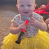 baby, child, toy, hammer, yellow_skirt, smiling, indoor, carpet, red_toy, playtime, cute, happy, person, short_hair, toddler, hand, clothing, sitting, floor, bright